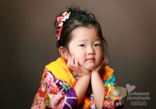 七五三のお祝い 女児の三つ詣り 黄色い被布を着て、頬杖をついているポーズ